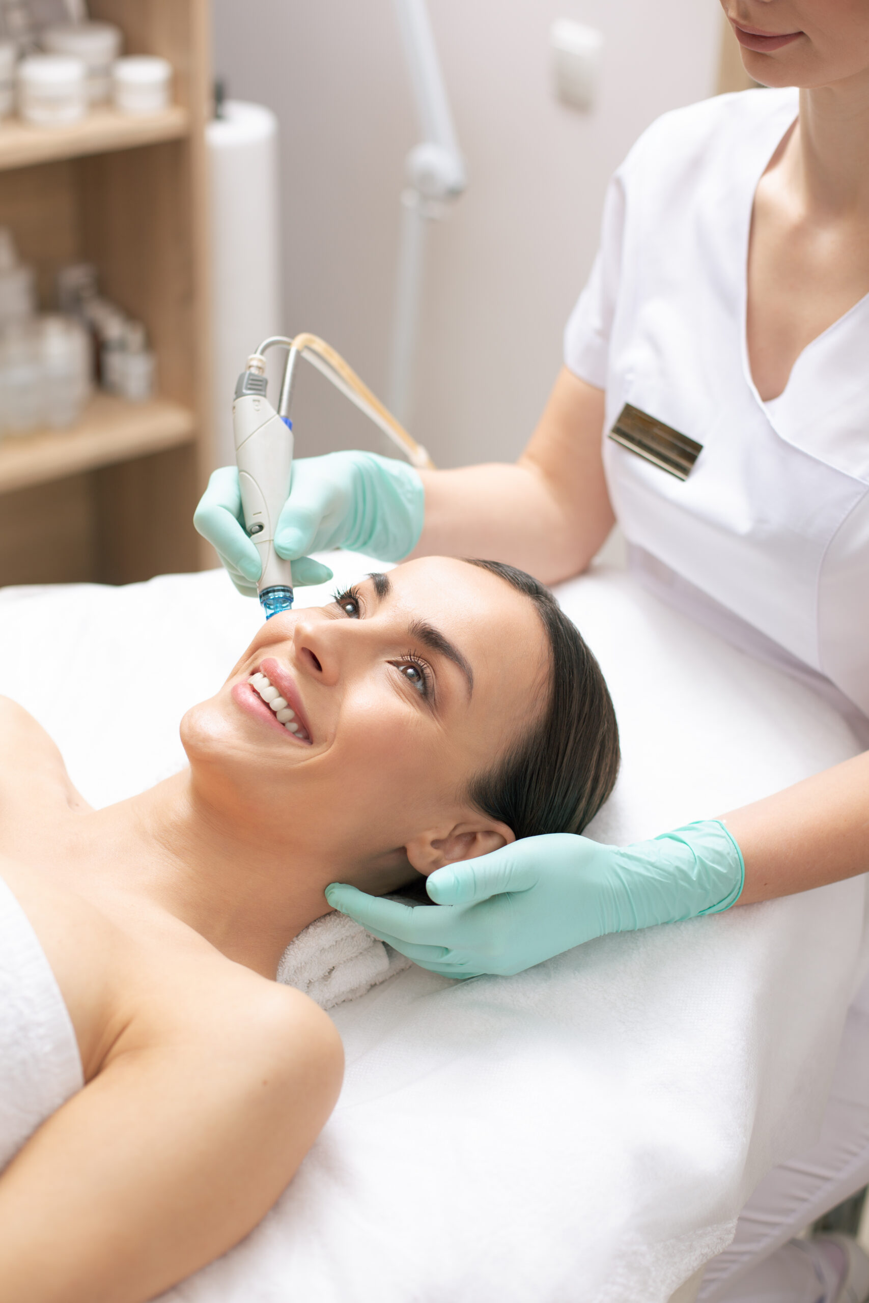 Smiling young woman enjoying the process of skin nourishment in modern clinic with a help of a special tool